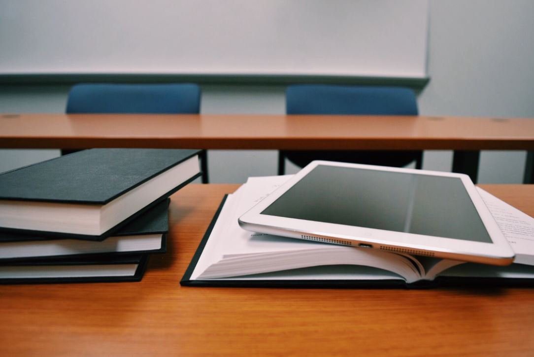 Image of a school desk with books and a tablet on top.