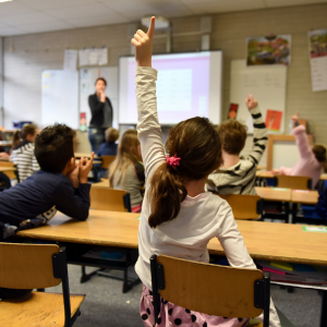Child putting her hand up in classroom to answer a question.